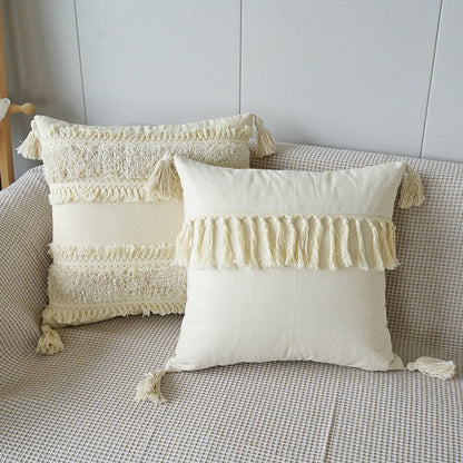 Two decorative pillows with tassels on a sofa against a neutral wall.